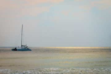 Barco navegando em alto mar com raios de sol no horizonte na água